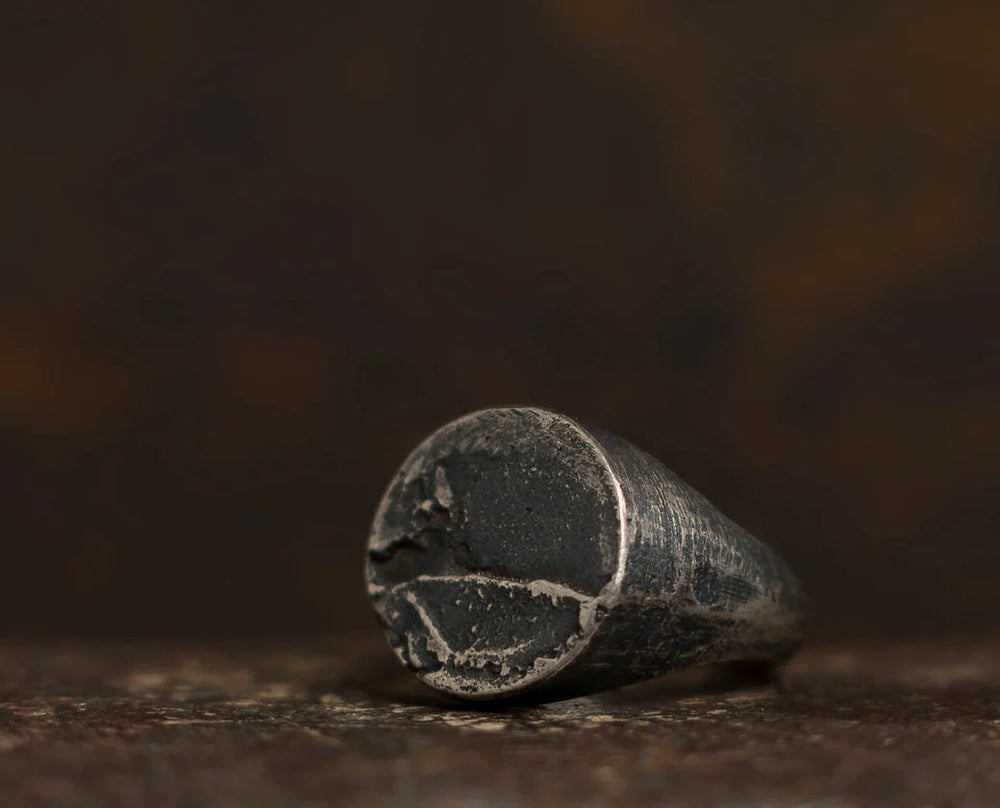 A close-up of an old, worn metal cylinder with a rough, cracked surface, lying on its side against a dark, blurred background—evoking the character and authenticity found in Septentrion’s Round Signet Ring, expertly crafted from 925 silver with true artisanal craftsmanship.