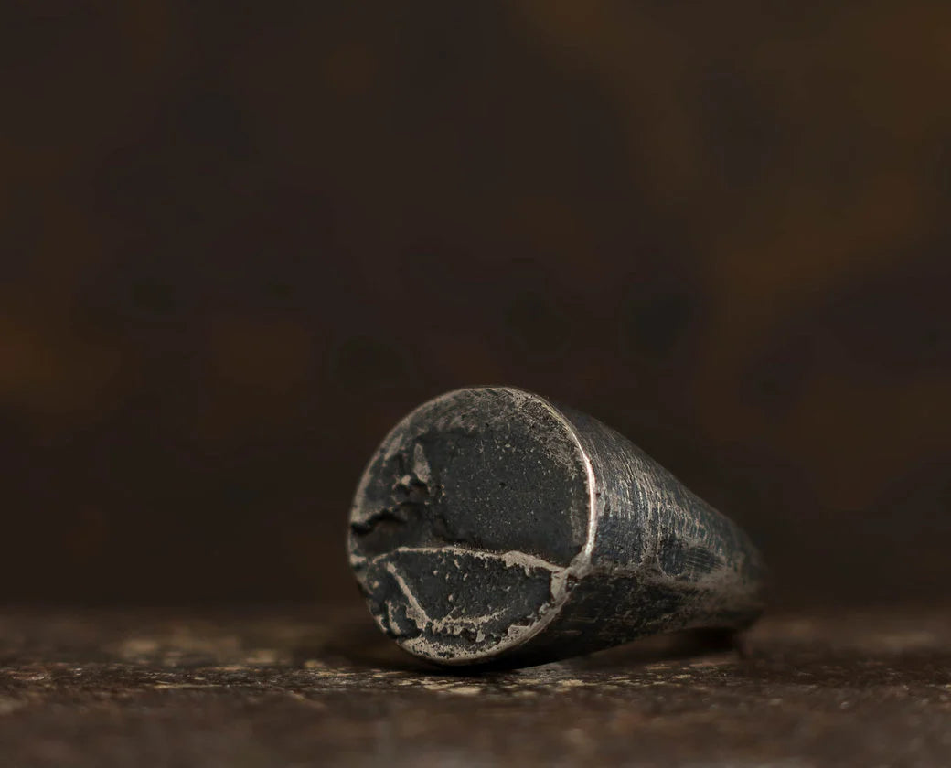 A close-up of an old, worn metal cylinder with a rough, cracked surface, lying on its side against a dark, blurred background—evoking the character and authenticity found in Septentrion’s Round Signet Ring, expertly crafted from 925 silver with true artisanal craftsmanship.