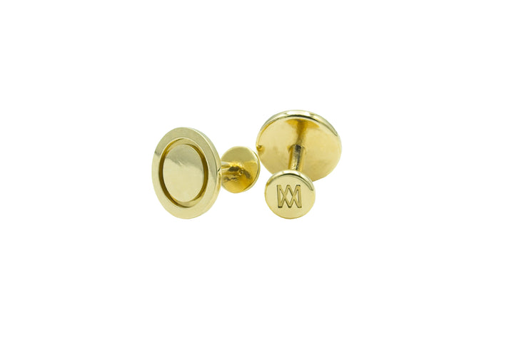 A pair of hand-finished, gold Round Cufflinks crafted from solid brass with a smooth, round design by Millett Wade. One cufflink faces forward, showcasing a circular pattern, while the other reveals its back with an engraved letter "M". Both cufflinks boast a shiny and polished finish.