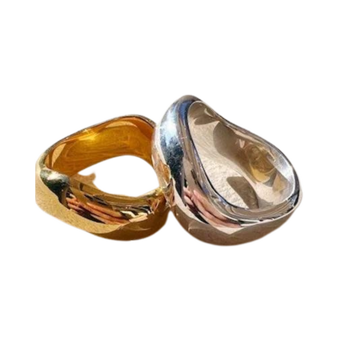 Two Rocco Rings by Shyla are displayed on a white background. The ring on the left is gold-toned with a smooth, slightly irregular surface. The ring on the right is silver-toned with a rounded, reflective design. These stackable rings boast a modern, minimalist style perfect for any occasion.