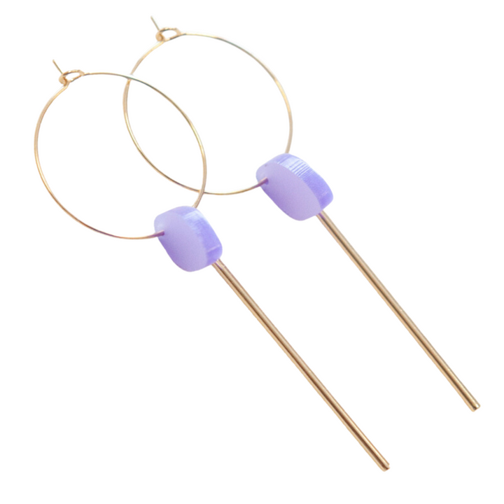 A pair of Smile 06 Earrings by Studio Nok Nok featuring thin gold-plated nickel-free brass hoops with light purple rectangular beads and long gold rods hanging from the center. The design is simple and elegant.