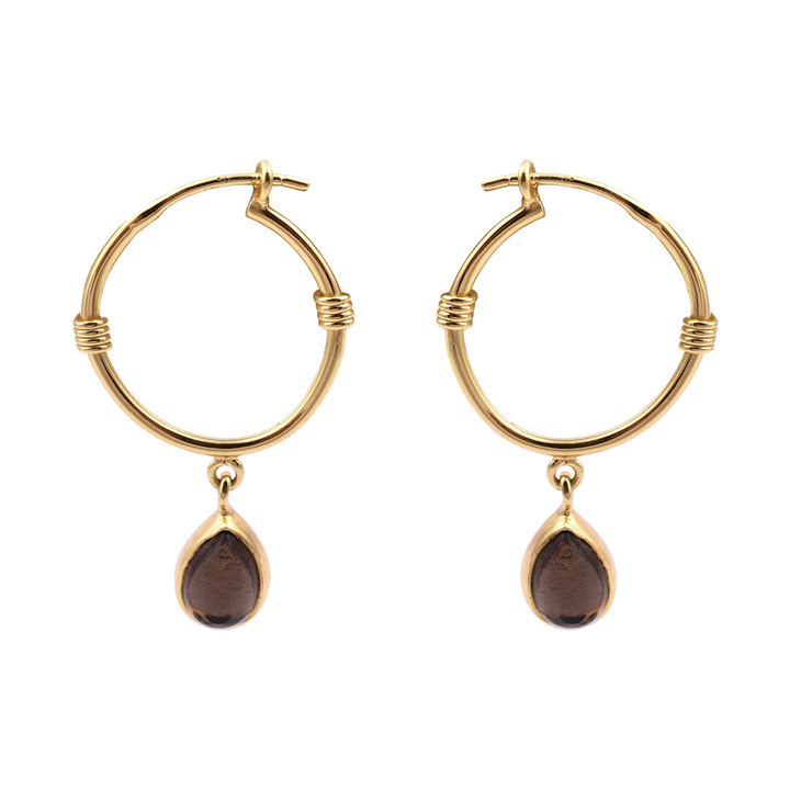 The Smoky Gold Dangle Hoops by Watermelon Tropical each feature a black teardrop-shaped gemstone dangle. The hoops are embellished with delicate wrap-around gold details near the top where the dangles are attached. This piece of handmade jewellery is arranged in parallel against a white background.