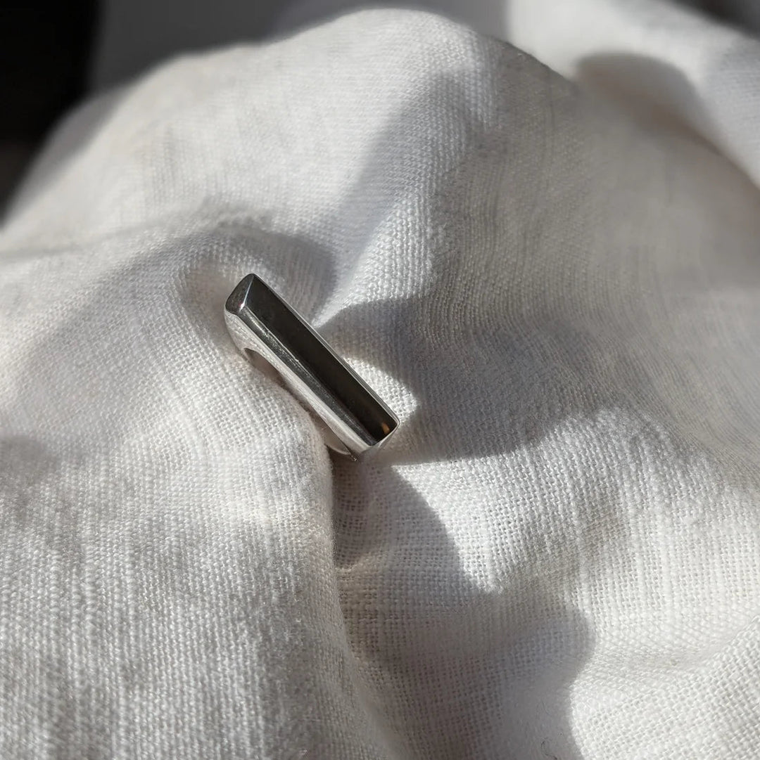 The Smooth Lines Chunky Ring by Becca Calmont, made from recycled sterling silver, stands upright on softly wrinkled white fabric, illuminated by natural light and casting gentle shadows.