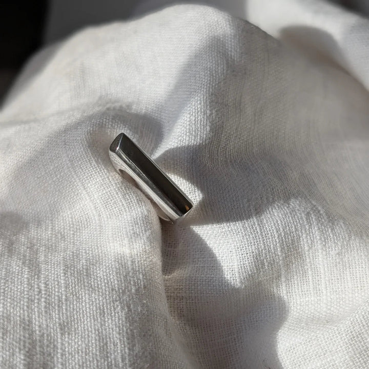 The Smooth Lines Chunky Ring by Becca Calmont, made from recycled sterling silver, stands upright on softly wrinkled white fabric, illuminated by natural light and casting gentle shadows.