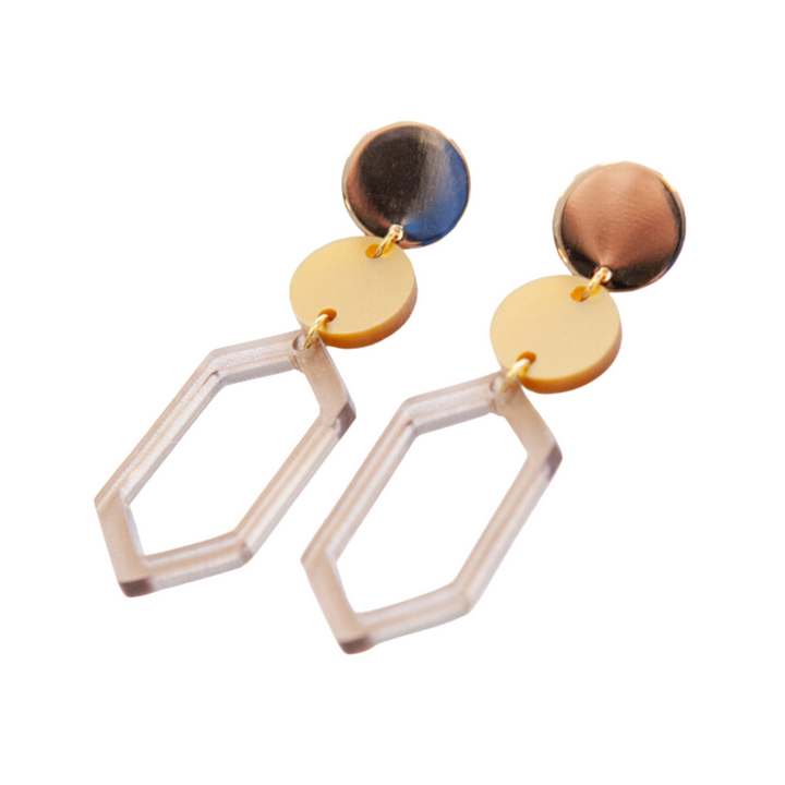 A pair of modern, gold plated Soul 04 Earrings from Studio Nok Nok with a geometric design. Each earring features a round, metallic gold stud connected to a round, matte gold disc, which hangs a clear hexagonal shape made from recycled acrylic. This stylish accessory embodies the beauty of handmade jewelry.