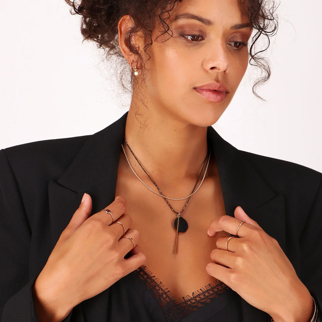 Woman wearing a black blazer with layered necklaces and rings on a neutral background
