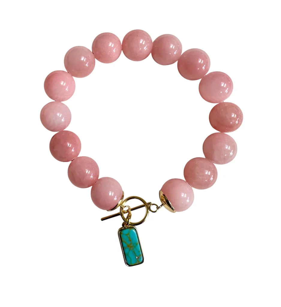 Introducing the Sunrise Bloom Bracelet by Aria V—a handmade piece from Dublin, showcasing large round pink chalcedony beads on a stretchy band, a gold toggle clasp, and a rectangular turquoise pendant with gold trim.