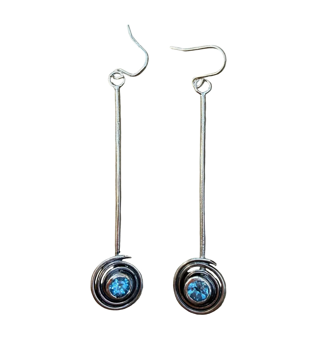 The Sun Seeker Spiral Drop Earrings in Blue Topaz by Caroline Stokesberry-lee are handmade silver earrings with circular swirl designs and blue topaz gemstones at the center, finished with simple hook fastenings.