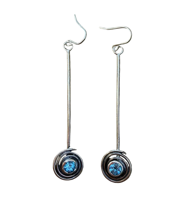 The Sun Seeker Spiral Drop Earrings in Blue Topaz by Caroline Stokesberry-lee are handmade silver earrings with circular swirl designs and blue topaz gemstones at the center, finished with simple hook fastenings.