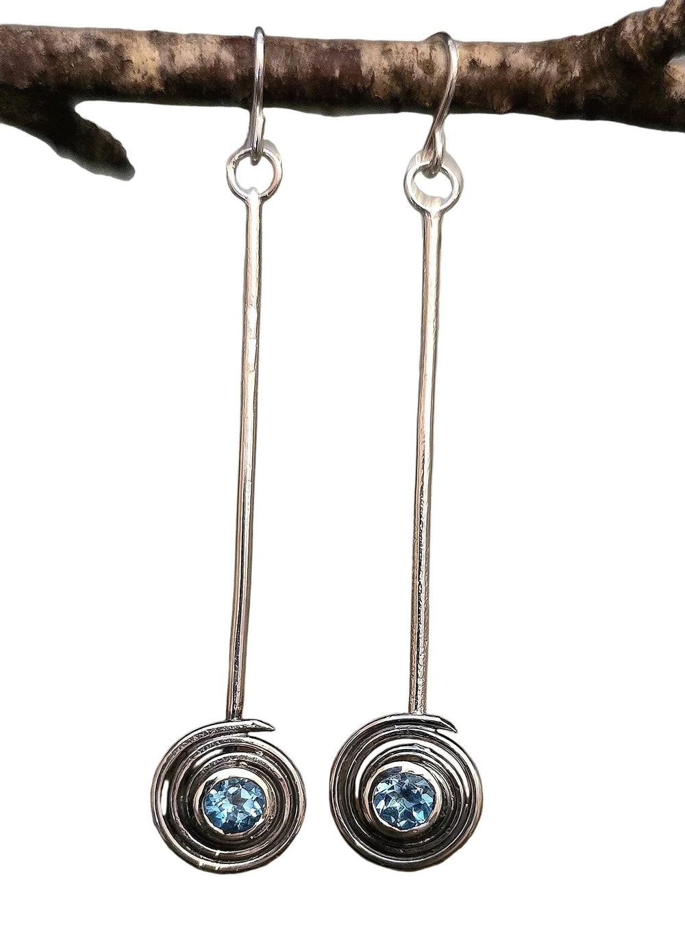 Silver earrings with blue gemstones hanging from a branch on a white background