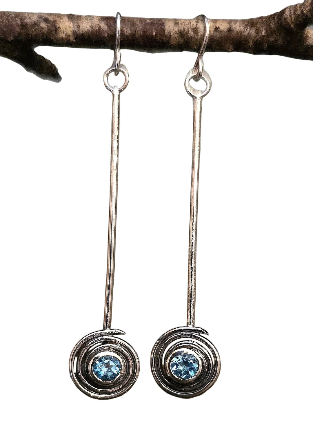 Silver earrings with blue gemstones hanging from a branch on a white background