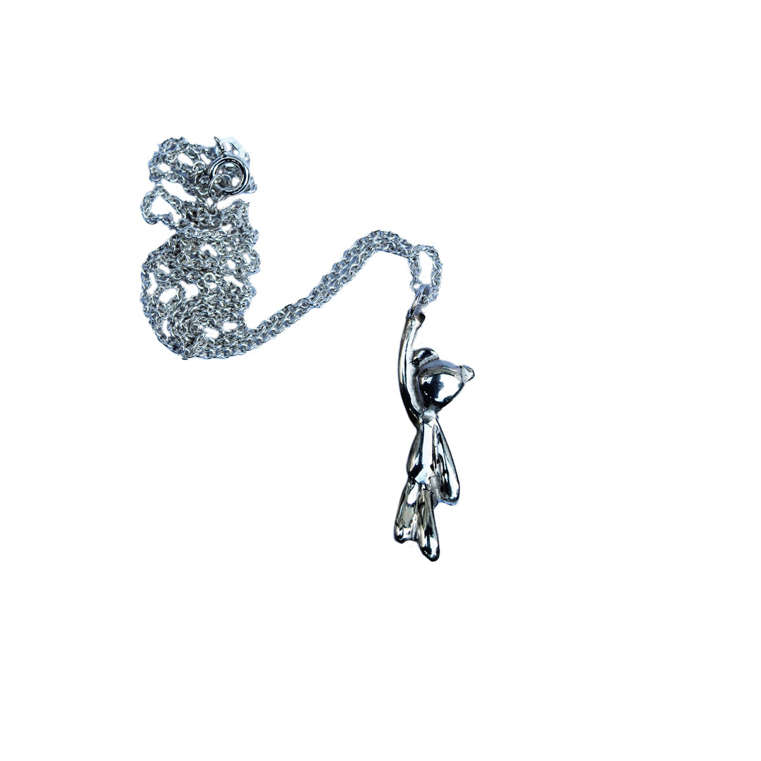 The Teddy Bear Silver Pendant by Kate Murphy features a sterling silver teddy bear charm hanging from one paw on a loosely coiled chain, offering a charming Good Luck jewelry piece against a white background.