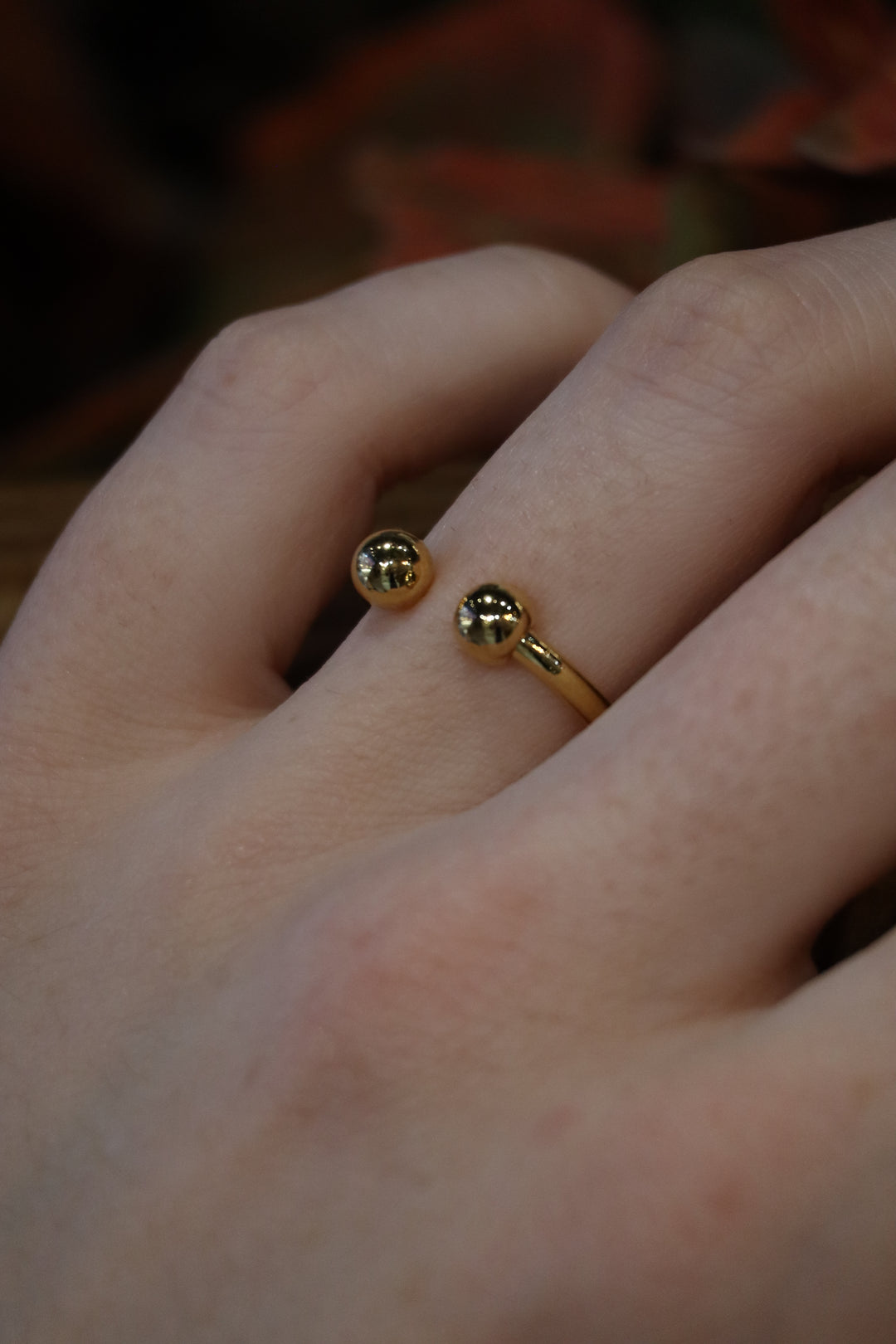 A close-up of a hand wearing the Zubeldia Torque Ring in Gold Plated Brass, featuring two polished golden balls—one by the knuckle, one near the joint—set against a blurred background.