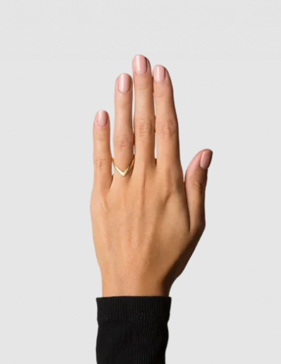 A hand with light pink nail polish wears the Jane Koenig V Ring in gold plated sterling silver on the middle finger. The background is plain and light gray, and the person is dressed in a long-sleeved black top.