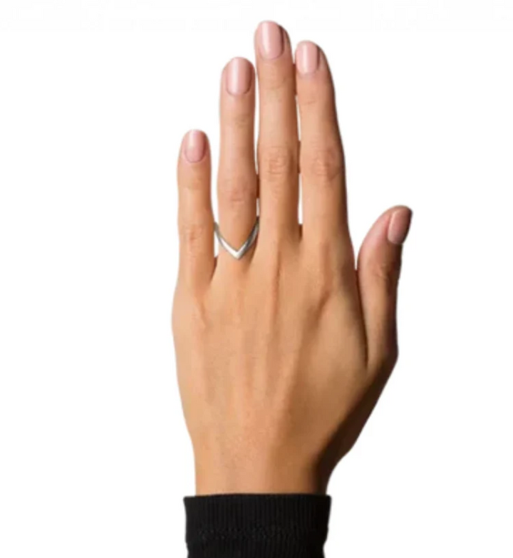 A left hand with light pink nail polish wears the Jane Koenig V Ring, styled in a signature sterling v shape, on the middle finger. The sleeve is black and the background is white.