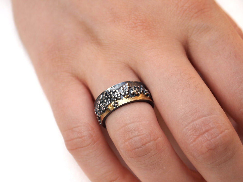 A close-up of a hand wearing the MarCucurella Wide Etrusc Ring, a textured two-tone silver and gold ring featuring a hammered or beaded surface, worn on the middle finger.