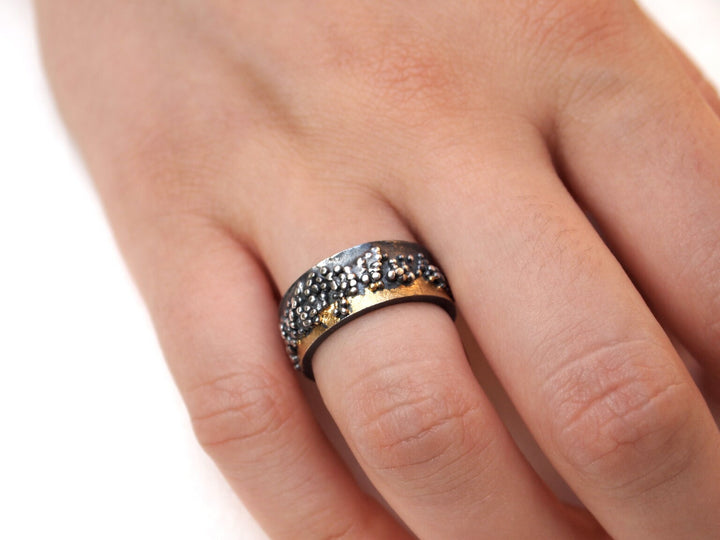 A close-up of a hand wearing the MarCucurella Wide Etrusc Ring, a textured two-tone silver and gold ring featuring a hammered or beaded surface, worn on the middle finger.