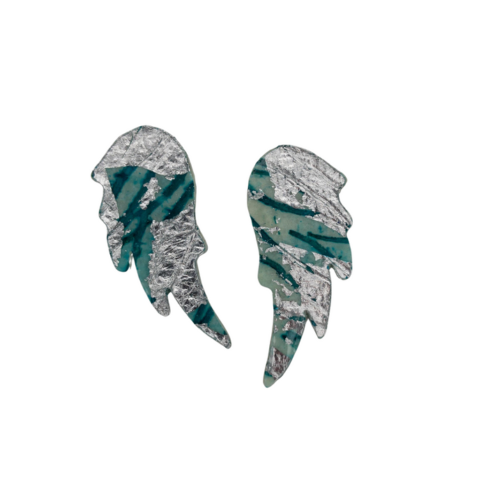 These Wings of Desire Sgraffito Stud Earrings by Rothlú feature abstract wing-shaped designs with a silver foil-like texture and teal green accents. The irregular, jagged patterns create a unique, artistic appearance. Finished with sterling silver posts, they stand out beautifully against the white background.