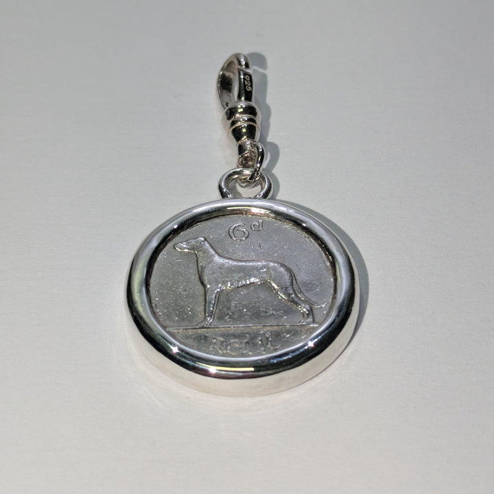 The Wolf Hound Silver Pendant by The Silver Rabbit features a circular Irish sixpence coin with a standing dog, set in silver and attached to a metallic clasp—an elegant, handcrafted jewellery piece shown on a light background.