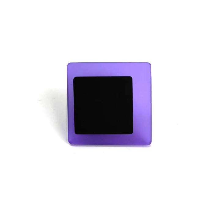 A small, square-shaped object with a purple frame and a black central area, viewed against a plain white background, reminiscent of the contemporary touch found in the Eriko Ring by Alex + Svet.