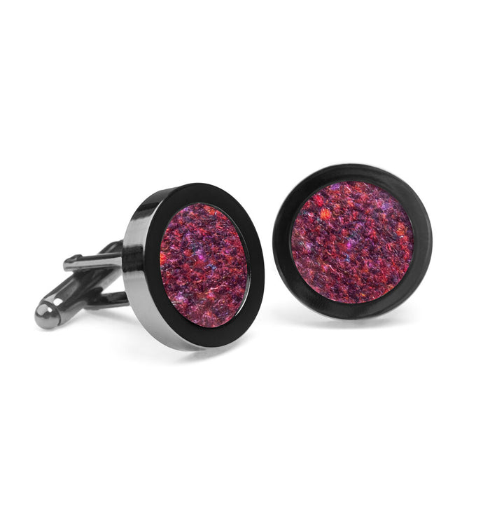 A pair of Speckled Burgundy Tweed Cufflinks from Orwell & Browne adorned with textured, multicolored red and purple Donegal tweed fabric inserts. The edges and backing are crafted from shiny black metal, offering a striking contrast. Displayed against a plain white background, they exude elegance while promoting sustainable fashion.