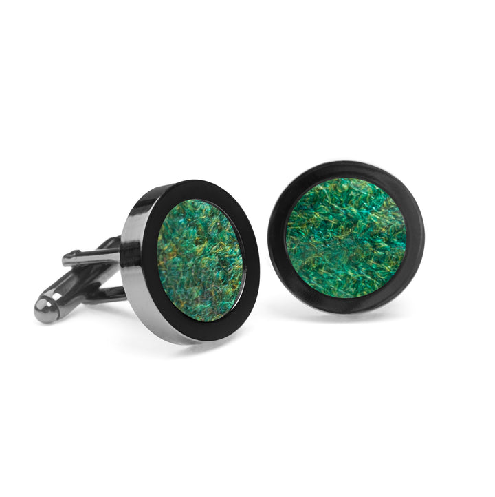 A pair of Forest Green Tweed Cufflinks by Orwell & Browne featuring circular green marbled insets framed in smooth black metal. The design is modern and eye-catching, ideal for accessorizing formal attire woven from Donegal tweed. The affordable and sustainable cufflinks are positioned side by side against a plain white background.