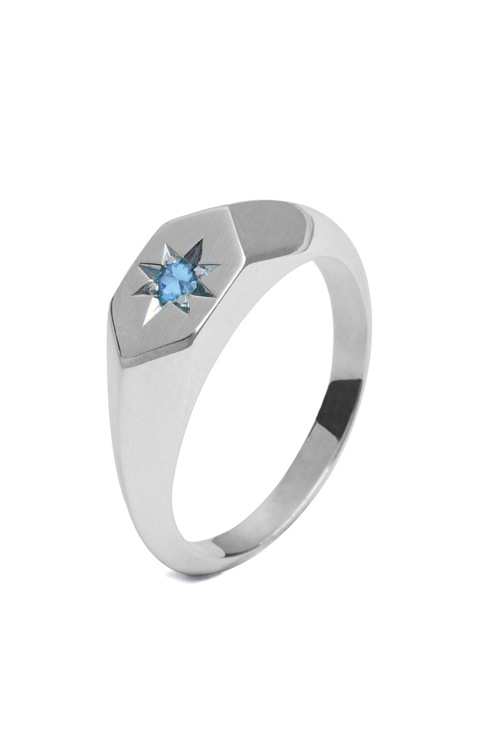 A Cosmic Boulevard Starlight Blue Zircon Birthstone Signet Ring with a hexagonal top featuring a small blue zircon gemstone embedded in the center, surrounded by an engraved starburst pattern, perfect for celebrating December birthdays. The ring has a smooth, polished finish.