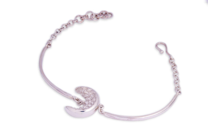 An At Piece Bracelet Silver by Aud featuring a crescent moon charm in the center. The crescent moon has a textured pattern, and the bracelet includes an adjustable chain clasp. The background is white, highlighting the intricate design of the jewelry piece.