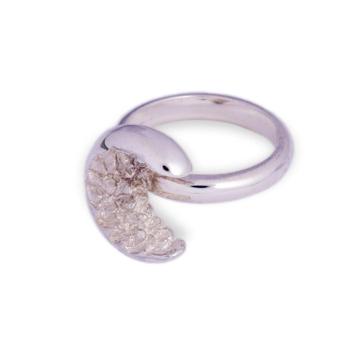 The At Piece Ring by Aud is a polished sterling silver ring featuring a distinctive design of a coiled pangolin. One end of the ring is crafted into the head of the pangolin, while the other end displays textured scales, giving the appearance of the animal wrapping around the wearer's finger.