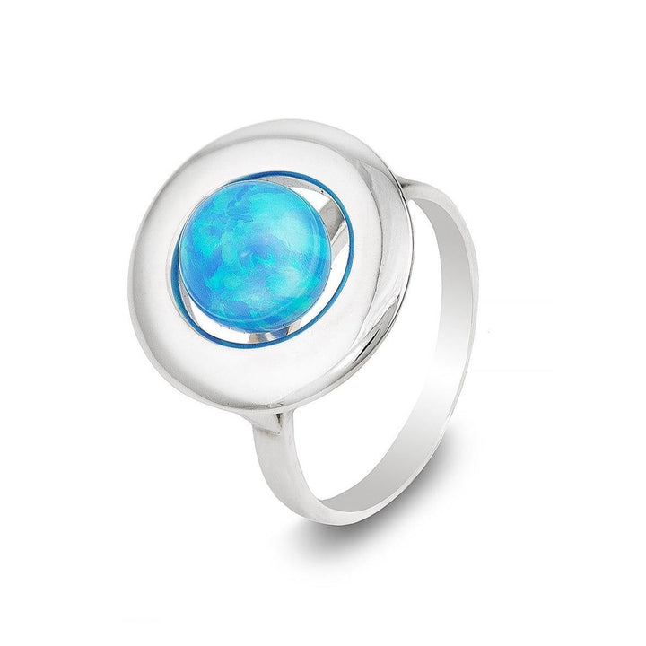 The Cosmic Boulevard Home Planet Blue Sky Opal ring features a polished sterling silver band and a round, iridescent opal gemstone set in the center. The opal boasts a vibrant play of colors, especially sky blues and greens, giving the ring an eye-catching appearance.