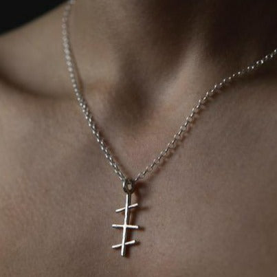 Close-up of a person's neck wearing a sterling silver chain necklace with a unique pendant. The pendant features a vertical line with three short horizontal lines intersecting it, reminiscent of Ancient Ogham writing, making it an ideal Mother’s Day gift: the Mam Small Pendant by Ogham Treasure.