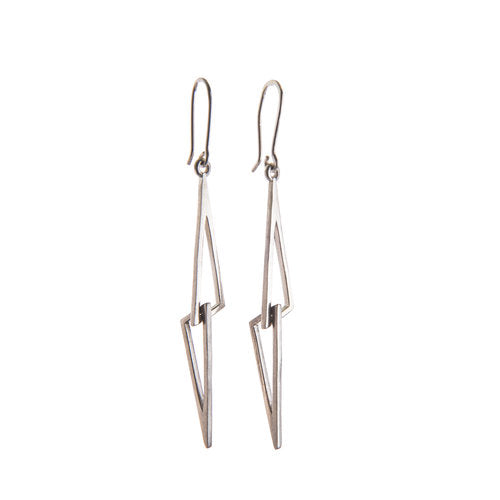 A pair of minimalist, Irish hallmarked sterling silver geometric earrings with angular, elongated triangular shapes. Each earring features a handmade earring hook for wearing. The design gives a modern, edgy appearance. The Le Cheile Drop Earrings Silver by Miriam Wade are displayed on a white background.