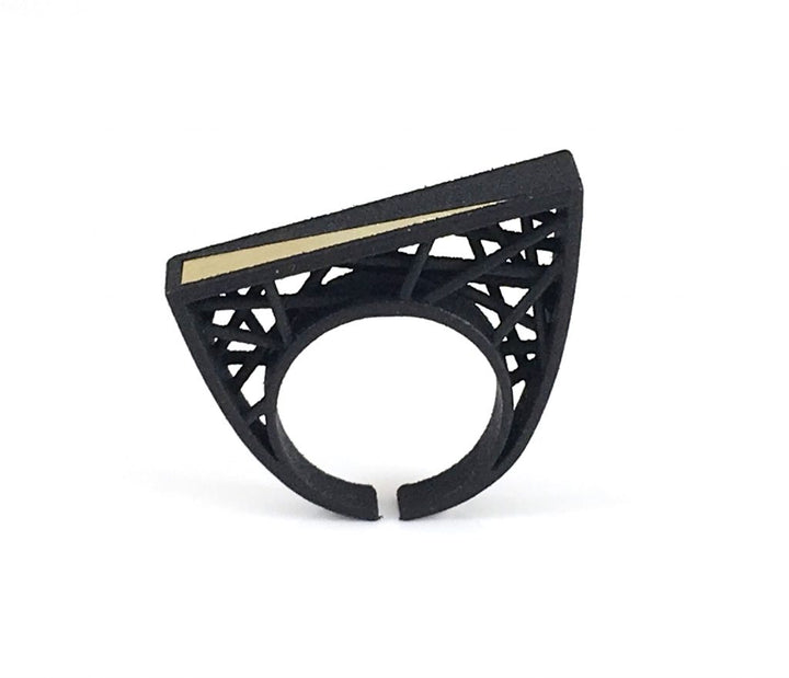 A modern black ring with an architectural design featuring open geometric patterns and a horizontal gold stripe on the top flat surface, the Hebo Statement Ring by Elsiem has a triangular shape with cut-out details, resembling a stylish, contemporary accessory akin to a Barbara Hepworth sculpture.