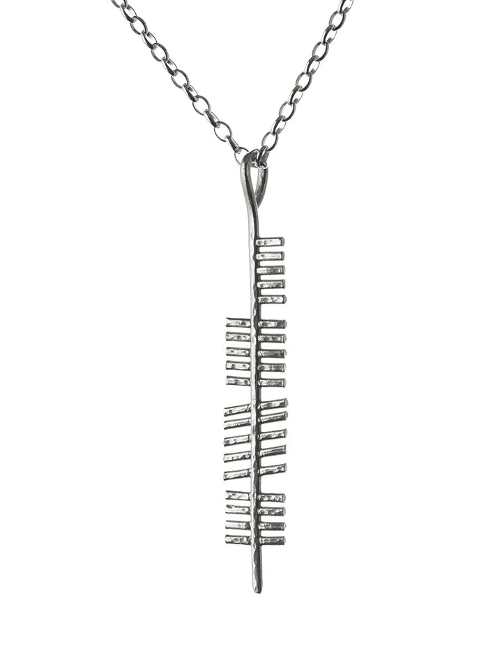 A sterling silver necklace featuring the Ireland (Erin) Pendant by Ogham Treasure with a unique vertical design. Intricate, ladder-like notches on either side create a modern and abstract appearance reminiscent of ancient Ireland. The pendant gracefully hangs from a simple chain.