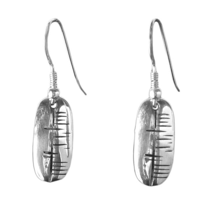 The Happiness (Sonas) Carved Earrings by Ogham Treasure are sterling silver earrings featuring vertically oriented oval pendants with inscribed linear patterns reminiscent of ancient ogham tally marks. The design exudes a blend of modern and rustic aesthetic, embodying a touch of Irish happiness.