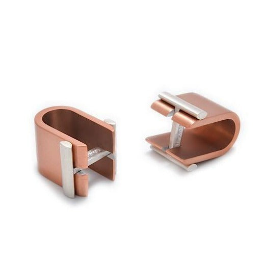 A pair of modern, U-shaped metal desk cable organizers in a copper finish. Each organizer features a silver horizontal bar similar to sterling silver anodized aluminium that secures cables in place, combining functionality with a sleek, minimalist design reminiscent of innovative Affinor Wrap Around Cufflinks by Filip Vanas.