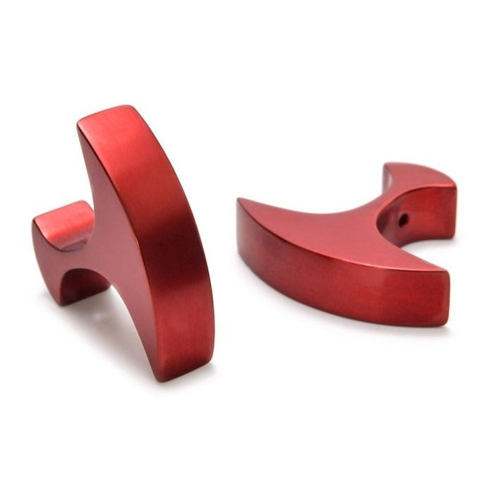 Two sleek, red anodized aluminum Secant Cufflinks by Filip Vanas are placed on a white surface. The objects have a polished finish and a modern design, featuring a curved blade and a squarish handle. Their unique shape and color make these cufflinks visually striking.