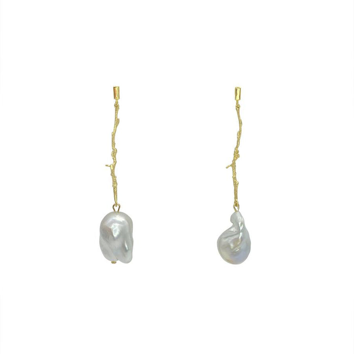 A pair of elegant drop earrings, known as White Medusa Earrings by Aria V, featuring elongated, gold-toned branches with irregularly shaped baroque pearls hanging at the ends. Handmade in Ireland, these earrings are set against a plain white background, showcasing a minimalist and modern design.