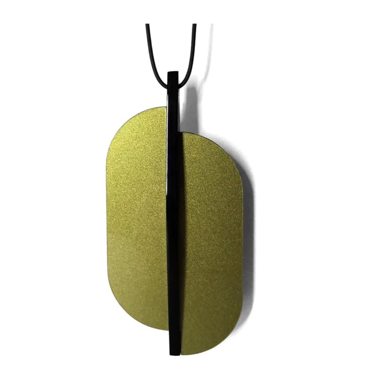 The Lars Statement Acrylic Pendant by Alex + Svet is a modern, minimalist piece of handcrafted jewelry featuring a vertical black bar bisecting an elegant gold, oval-shaped plate. It hangs from an adjustable thin black cord made of high-quality frosted acrylic, casting a subtle shadow against a white background.