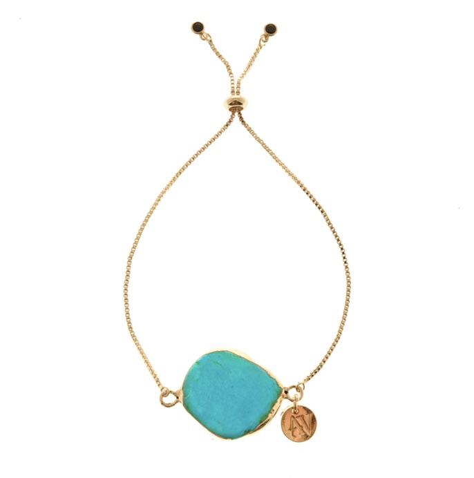 A delicate gold Juno bracelet by Aria V featuring a centerpiece of a flat, oval-shaped turquoise stone. The adjustable bracelet boasts a sliding knot closure, adorned with two small gold beads. A small, round gold charm with an engraved design hangs next to the stone on its gold plated brass chain.