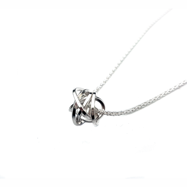 The Knot Pendant Silver by Caroline Stokesberry-lee is a sterling silver necklace with a unique pendant designed as an abstract spherical knot. The intricate, handmade pendant is suspended from a delicate silver chain, creating a modern and elegant piece of jewelry against a white background.