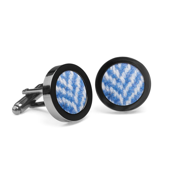 A pair of silver cufflinks with round blue and white fabric inserts reminiscent of Donegal tweed, featuring a herringbone pattern. The Stippled Cornflower Tweed Cufflinks by Orwell & Browne are displayed on a white background.