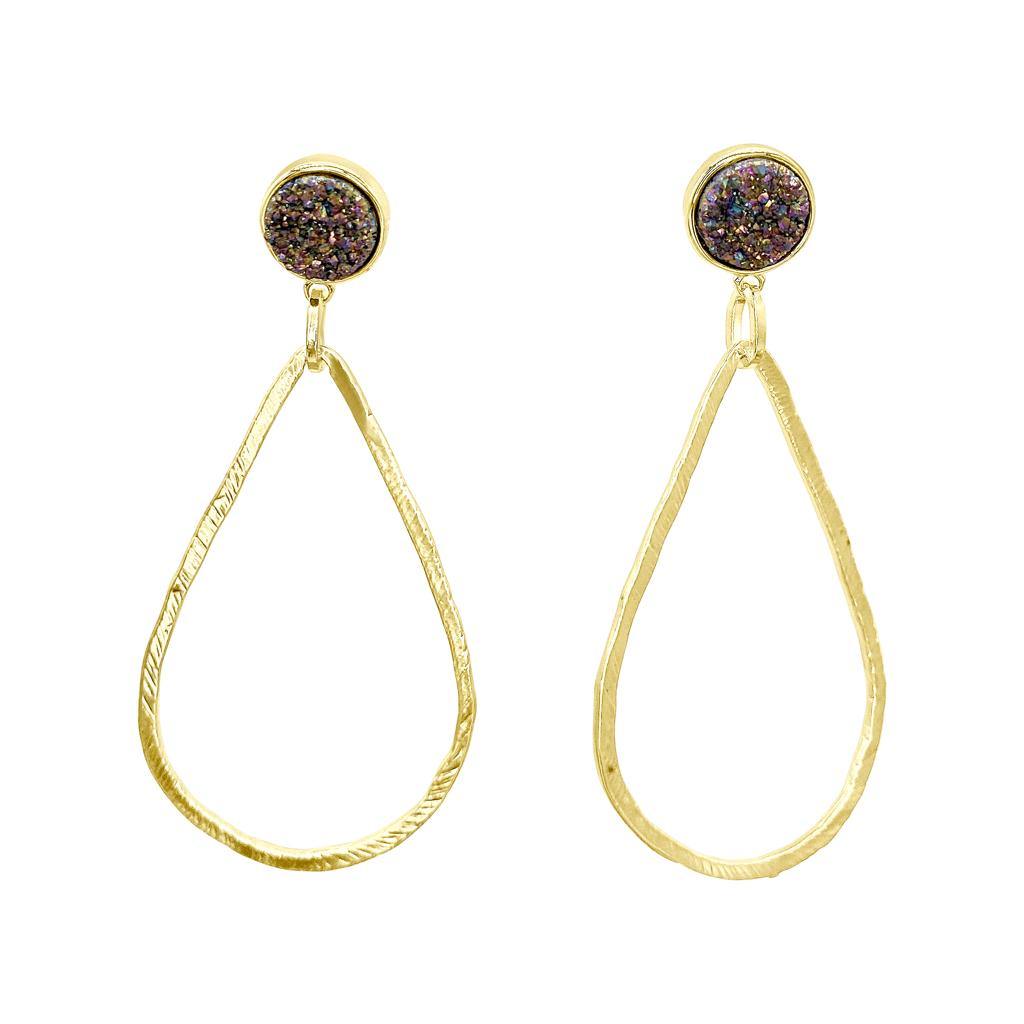 The Pixi Earrings by Aria V are a pair of 24k gold plated brass earrings featuring a round stud with multicolored glitter. Dangling from the stud is a large, teardrop-shaped hoop with a textured finish. The design combines elegance with a touch of sparkle.