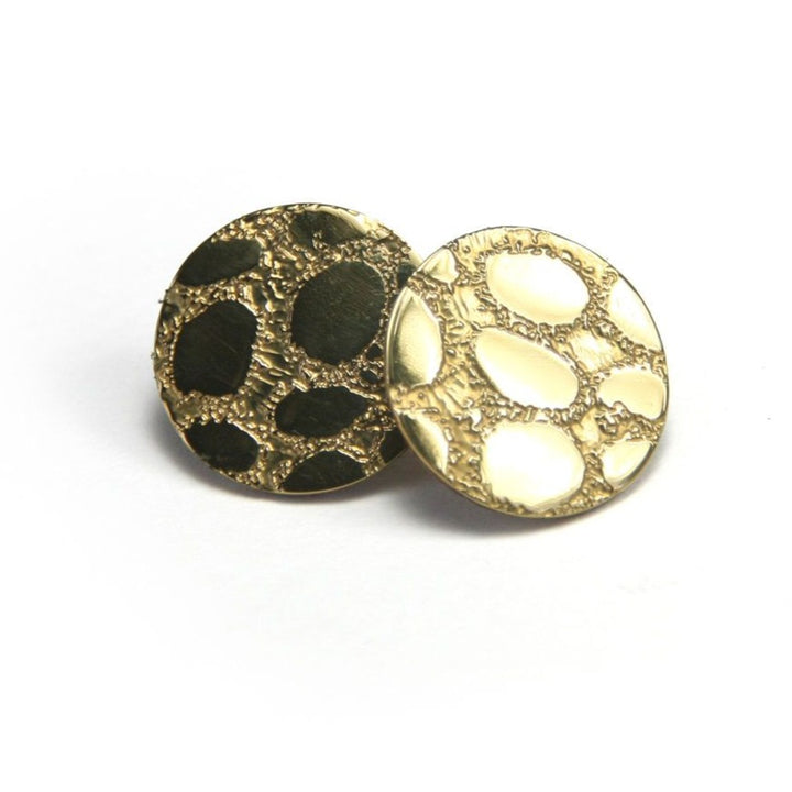 A pair of round stud earrings from Sara Gunn called the Etched 'Skin' Stud Earrings (Silver or Gold), featuring a textured, organic pattern on the surface. One earring has a shiny gold appearance, while the other showcases sterling silver elements interspersed within the pattern. They are displayed side by side on a white background.