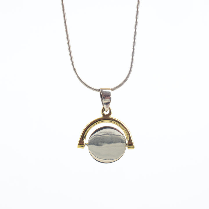 A necklace with a pendant hanging from an adjustable chain is displayed. The pendant features a circular, reflective silver center encased in a gold, semicircular frame. The design is minimalistic and modern, offering a blend of elegance and simplicity. This piece is known as the Sterling Silver Spinning Disc by Engravable Jewellery.