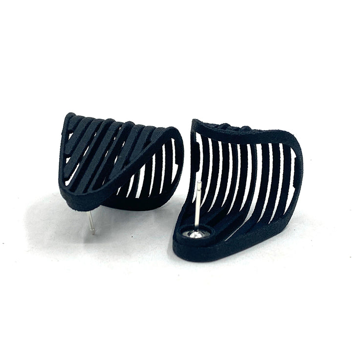 A pair of black 3D printed earrings with a modern, openwork design featuring parallel slats. The Vibe Grill Earrings by Elsiem are curved and have small, sterling silver ear posts to secure them in place. They are displayed against a plain white background.