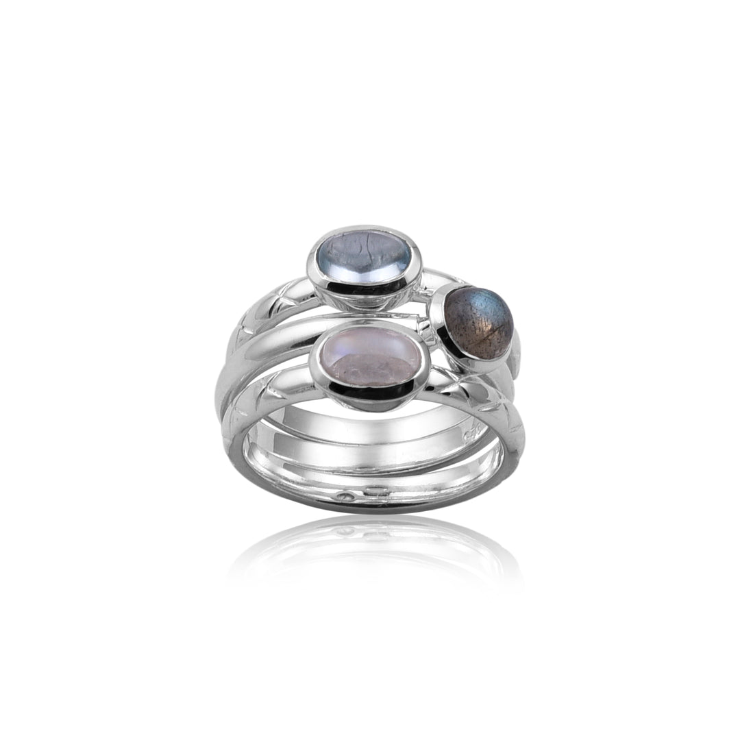 A Triple Stack Silver Rings with multiple bands featuring three round gemstones of varying shades of blue and gray by Watermelon Tropical. This piece of handmade jewellery showcases the stones in a polished bezel setting, offering an elegant, contemporary design. The reflection of the rings is visible beneath them.