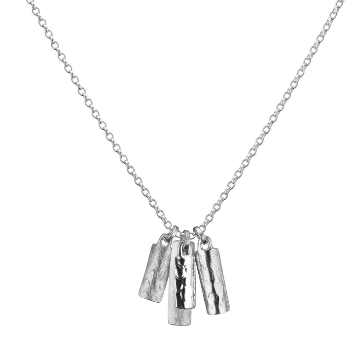 A delicate silver necklace with a simple chain features five hammered Sterling silver pendants hanging from it. The rectangular and slightly curved pendants have a textured finish, creating a minimalist yet elegant design, epitomizing the art of handmade jewellery. This is the Muir Cluster Pendant by Lynsey de Burca.