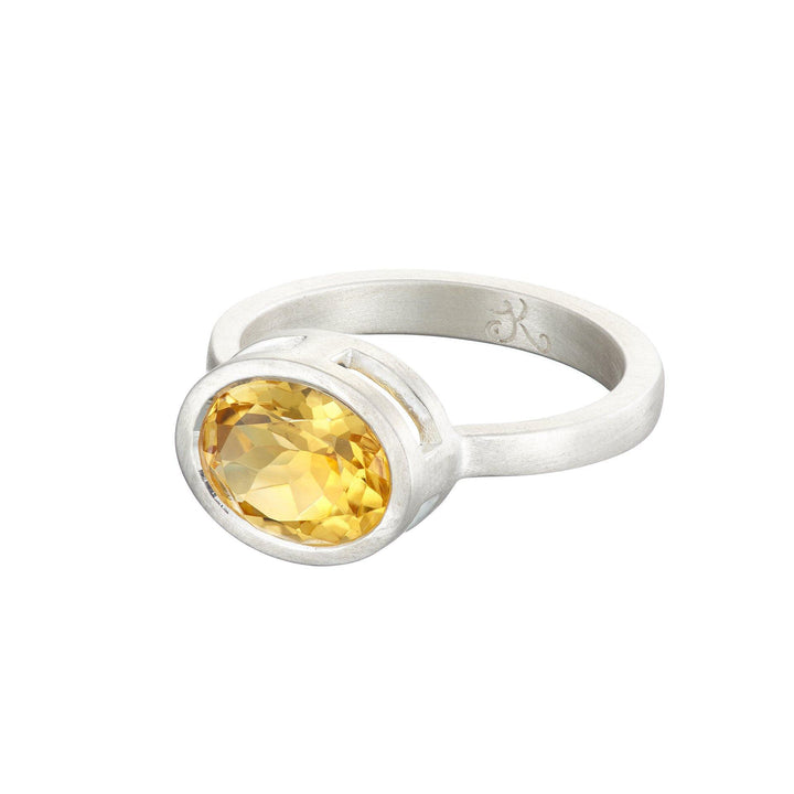 A Jennifer Kinnear Citrine Pirate Ring In Silver with a large, oval-shaped citrine gemstone set in a bezel setting. The band is simple and polished, accentuating the vibrant, faceted gemstone that catches the light. This exquisite piece showcases the impeccable craftsmanship of an Irish designer.