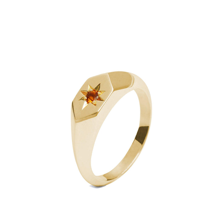 A handcrafted Starlight Palmeria Citrine Birthstone 9ct Gold Signet Ring by Cosmic Boulevard, made in Dublin, showcases a hexagonal face with a sunburst design centered around a small, round orange gemstone. The polished band is available in 9ct yellow or rose gold.